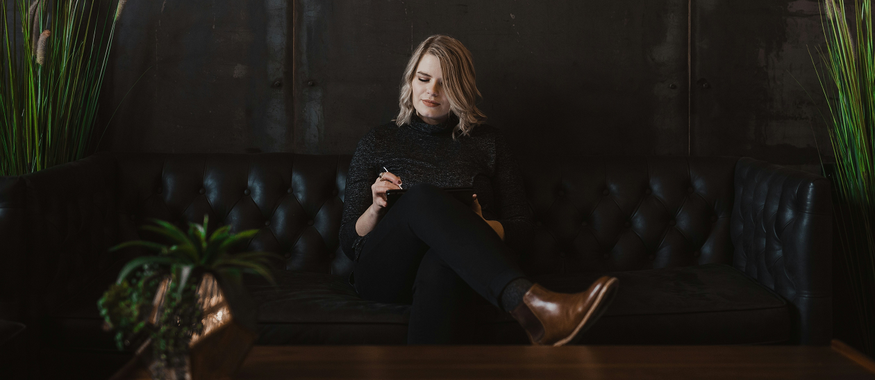 Alt Text: A woman casually sits on a couch while using her iPad.